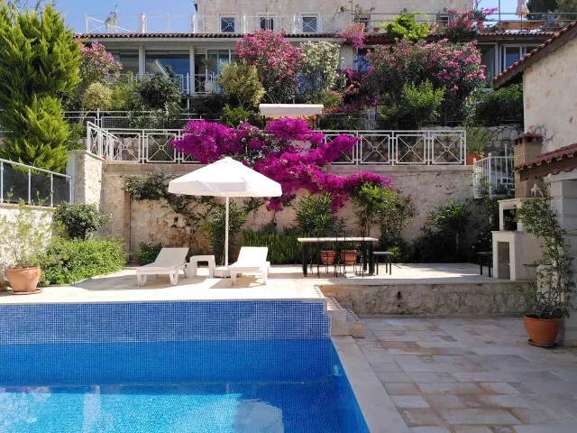 BookNoFees: brīvdienu māja, Kalkan, Kas, Antalya, Antālija, Turcija – Terase pie baseina ar saules krēsliem, saulessargu un ziedošām bugenvillijām uz akmens sienām