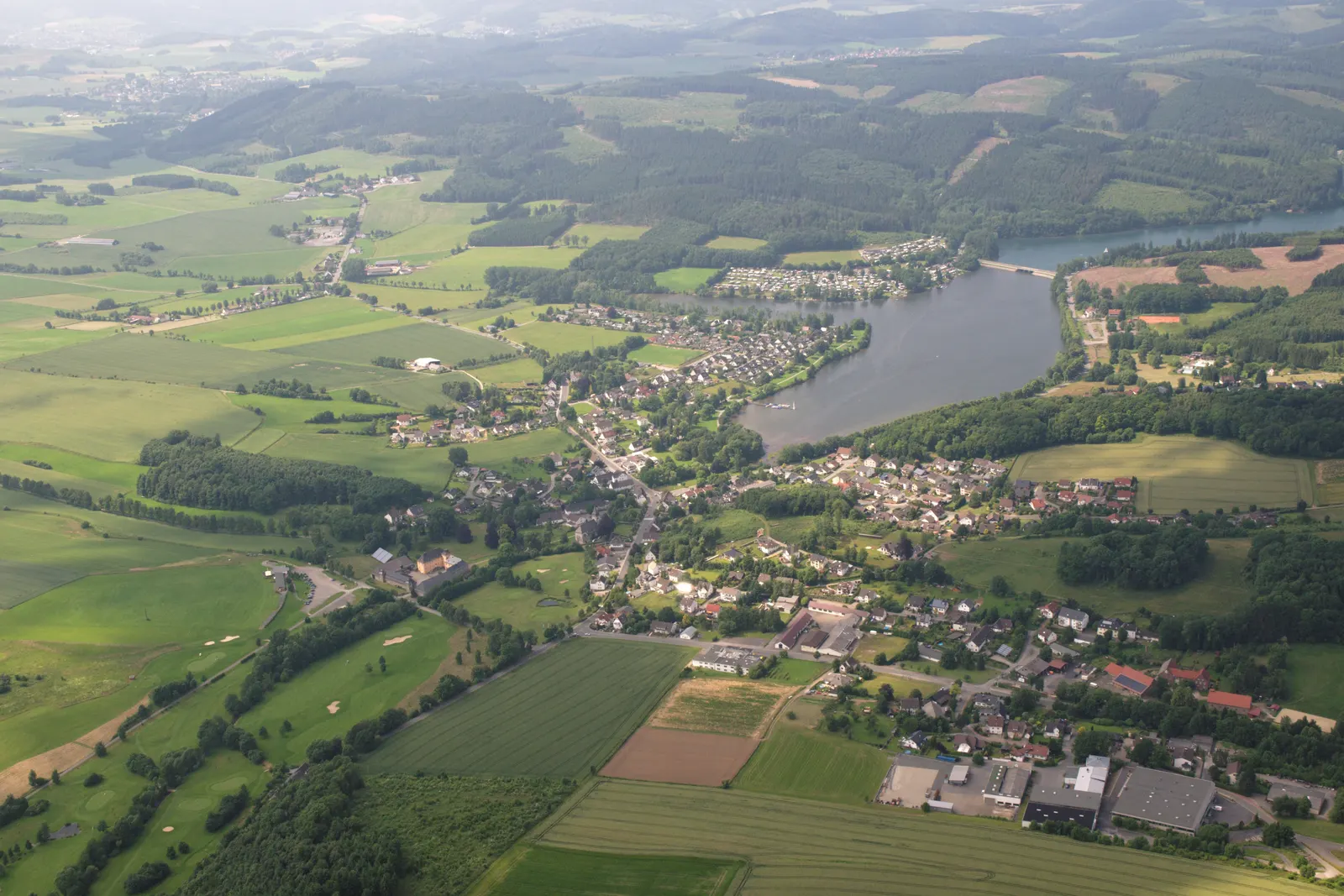 Sorpesee no gaisa, ar Amecke ciemu tā austrumu krastā un mežainajiem Sauerlandes pauguriem ap to