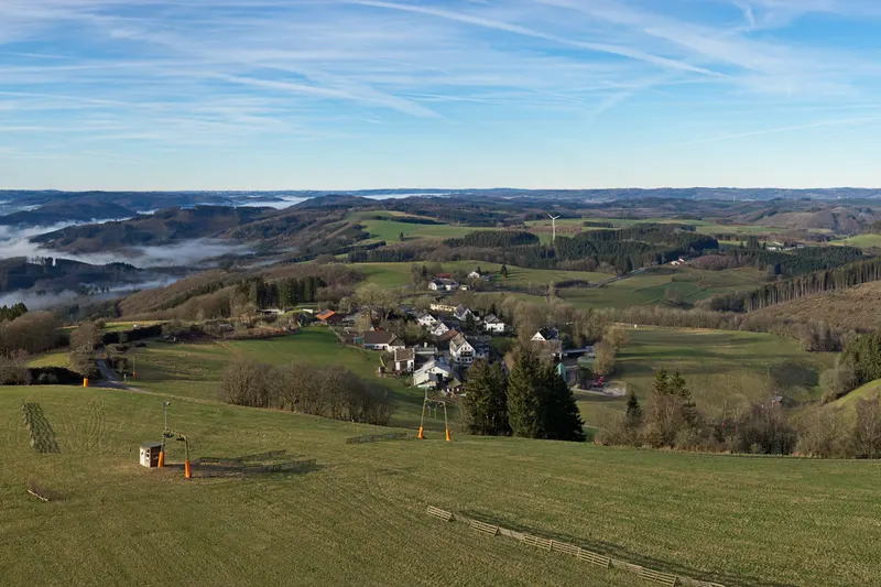 Vildevīze Sauerlandes kalnos, ar slēpošanas pacēlāju pļavā un ciematu zemāk